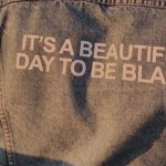 photo showing the back of a person wearing a denim jacket embellished with the words it's a beautiful day to be black.